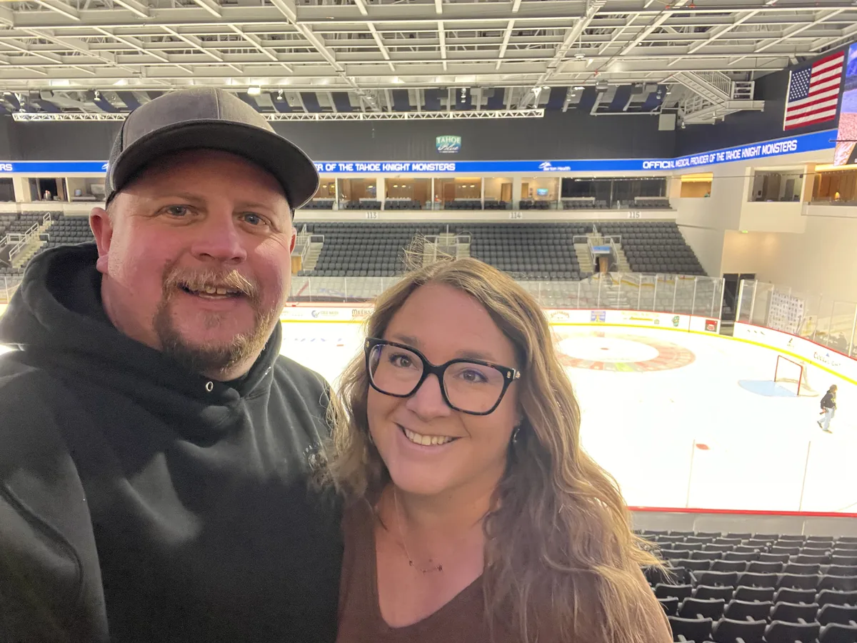 Kylie and Trevor smiling in a selfie in the stands of an indoor ice hockey arena