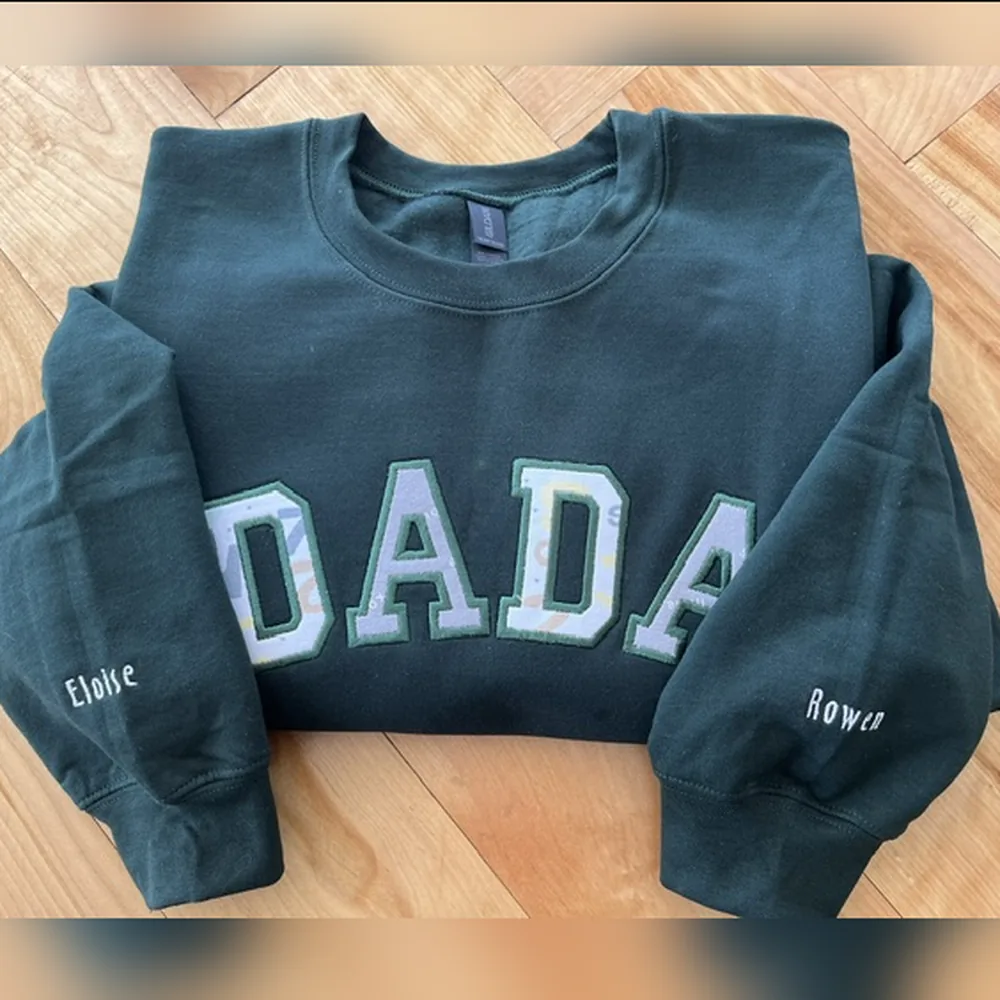 Forest green crewneck sweatshirt with DADA in patterned appliqué letters and kids’ names embroidered on the sleeves.