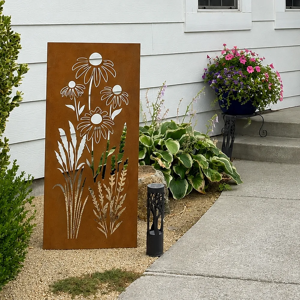Rusted steel garden panel with daisies and wild grasses, standing in a garden bed.