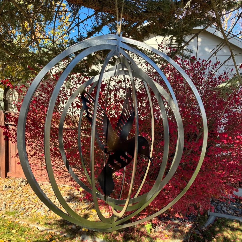 Metal spinner of nested rings with a hummingbird cut-out in the center, hanging from a tree.