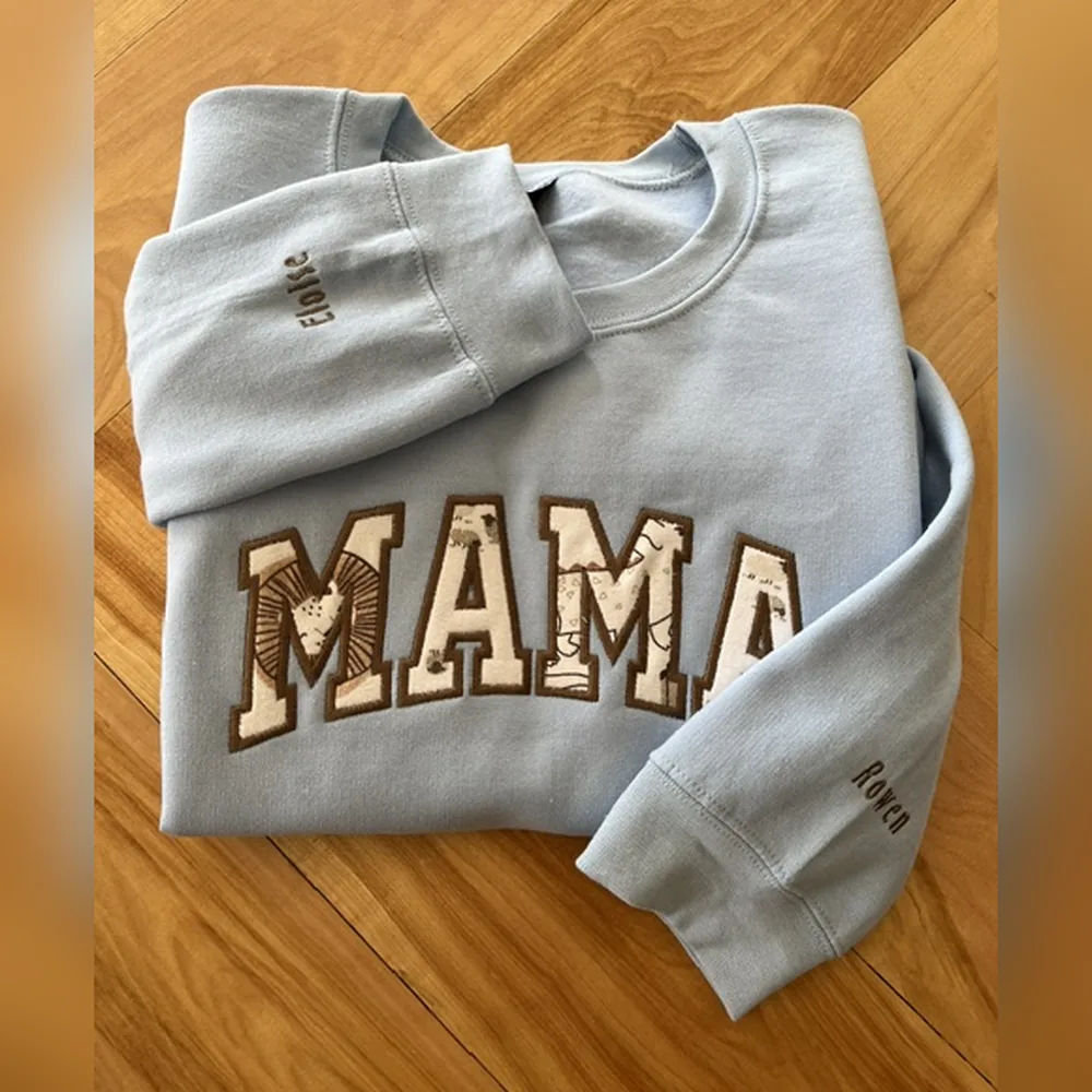 Light blue crewneck sweatshirt with MAMA in patterned appliqué letters and kids’ names embroidered on the sleeves.