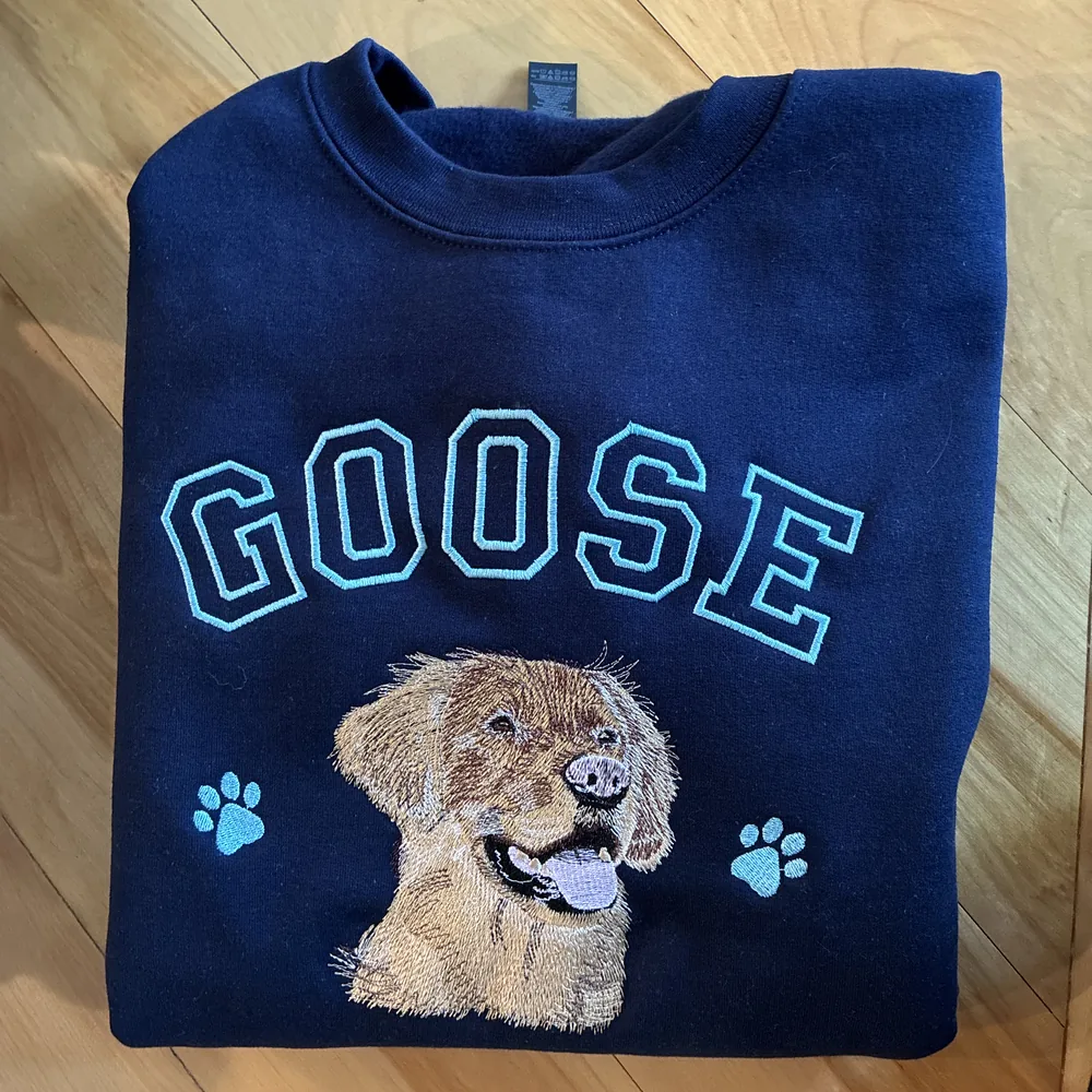 Navy crewneck sweatshirt with GOOSE in outlined light blue letters over an embroidered golden retriever portrait and two paw prints.