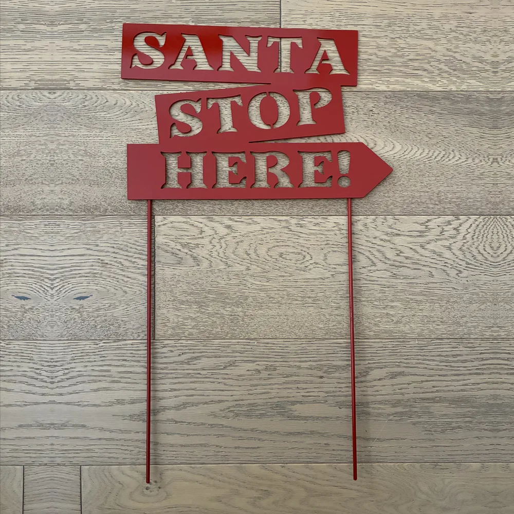 Red metal stacked arrow signs reading SANTA STOP HERE! on two stakes.