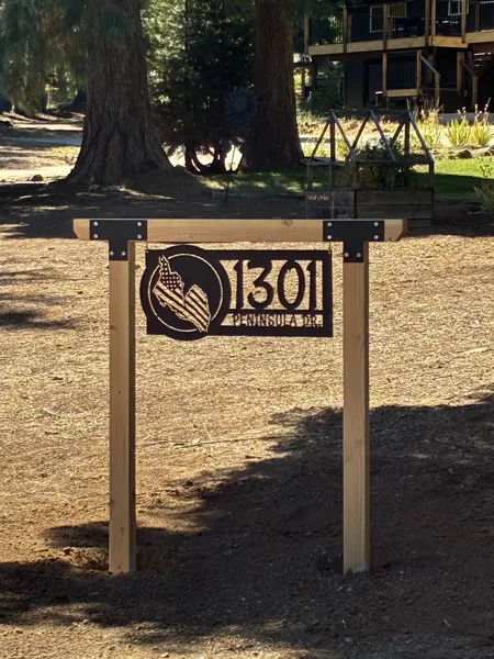 Black steel address sign with a flag design hanging from a wooden post frame