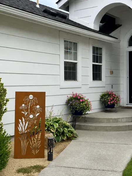 Tall rusted-steel garden panel with a daisy and wildflower cutout beside a house entry